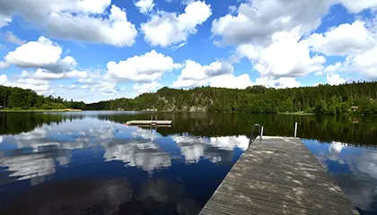 Spegelblank sjö där molnen speglar sig och brygga som ligger i sjön