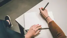 Person håller i penna o skriver i ett block