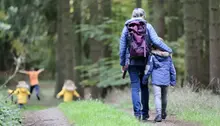 Bild bakifrån på vuxen och barn som går i skogen och håller om varandra