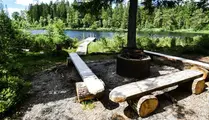 Grillplats vid sjö med träbänkar runt och brygga ut i sjön
