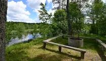 Grillplats med träbänkar runt som ligger med utsikt över sjö i skogen
